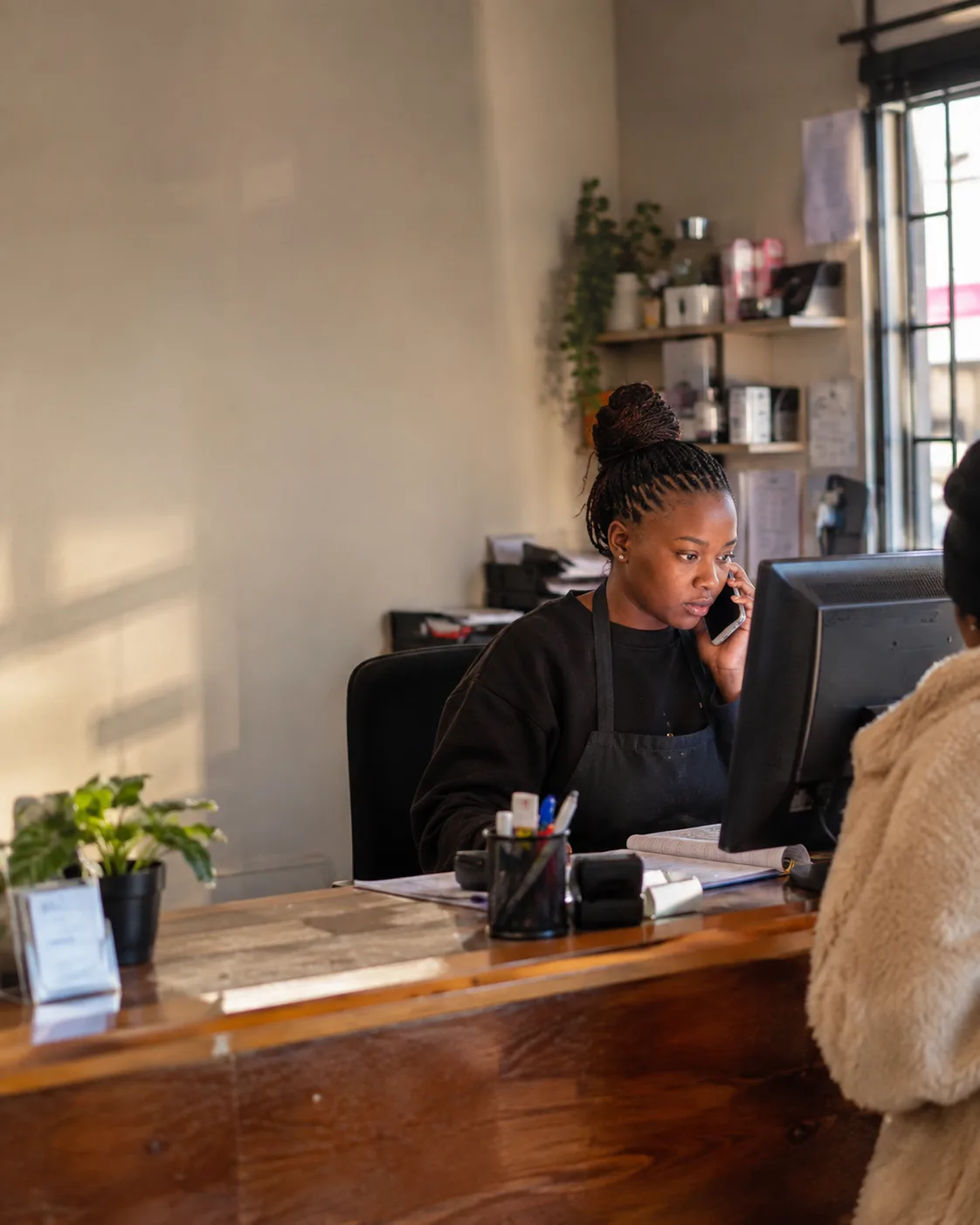A receptionist at a wooden front desk taking a call while a customer waits